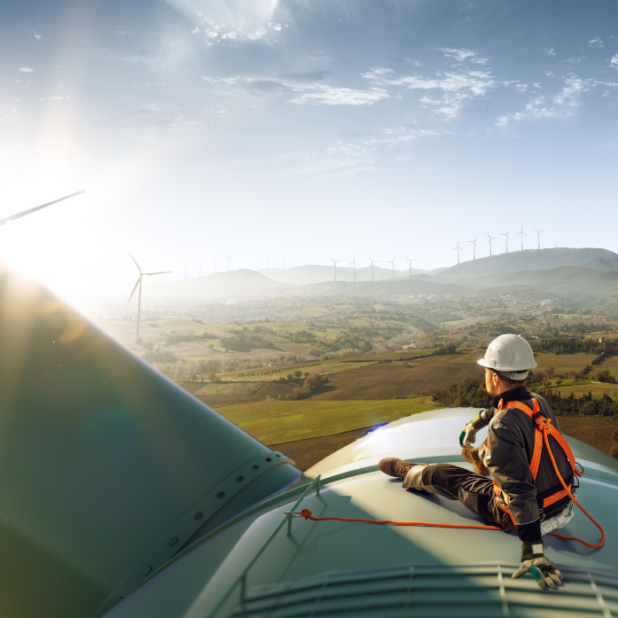 Happy engineer feel success after good work. He standing a top of windmill and looking beautiful sunset