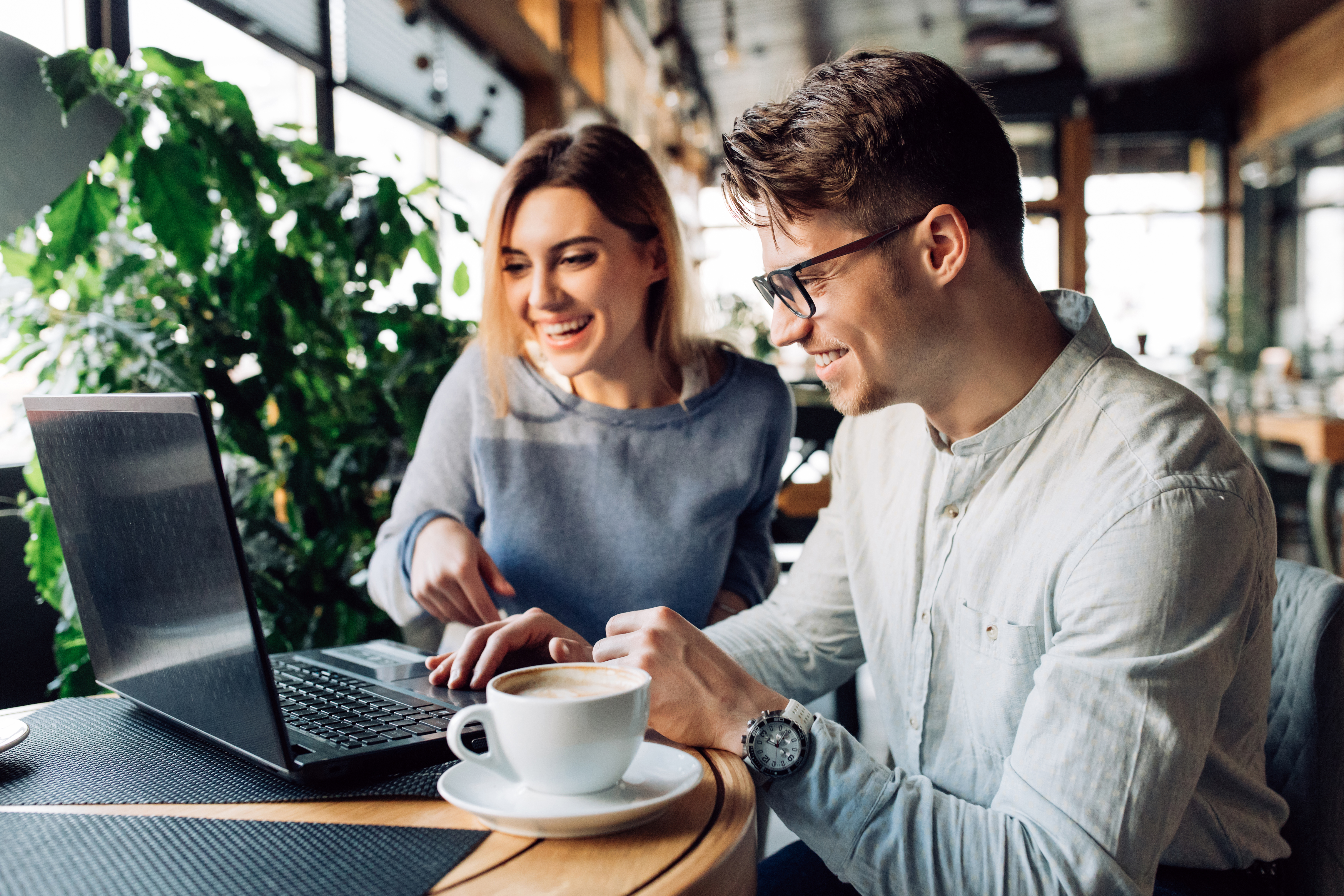 Young couple spending time with fun sitting at cafe with laptop