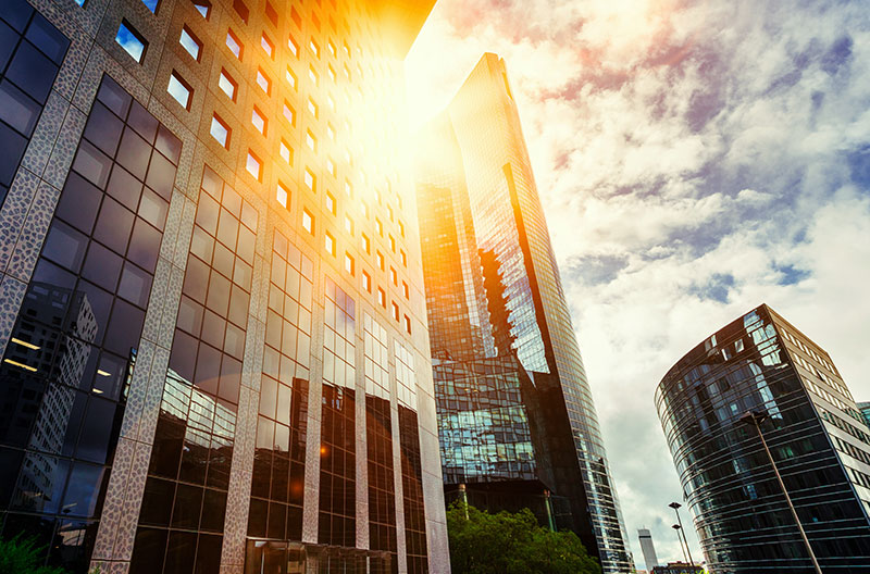 Skyscraper glass facades on a bright sunny day with sunbeams in the blue sky. Modern buildings in business district. Economy, finances, business activity concept. Bottom up view